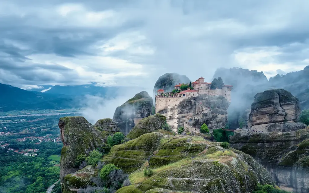 Amazing panoramic view with the majestic Varlaam Monastery amid creeping mists in the Meteora Valley near Kastraki, Greece