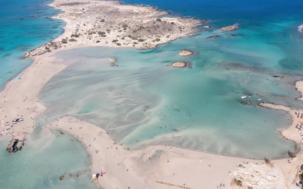 Elafonisi lagoon, Crete island Greece. Aerial drone view of turquoise transparent sea water, rocky formation, blue sky, beach with pink sand.